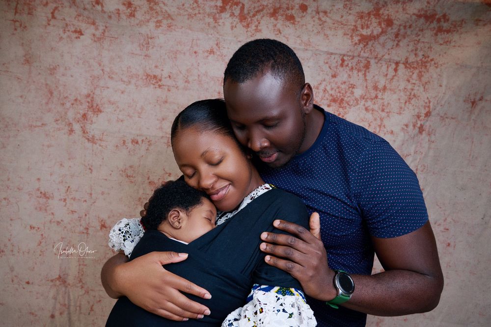 Intimate family moment with baby in carrier against textured red wall background.