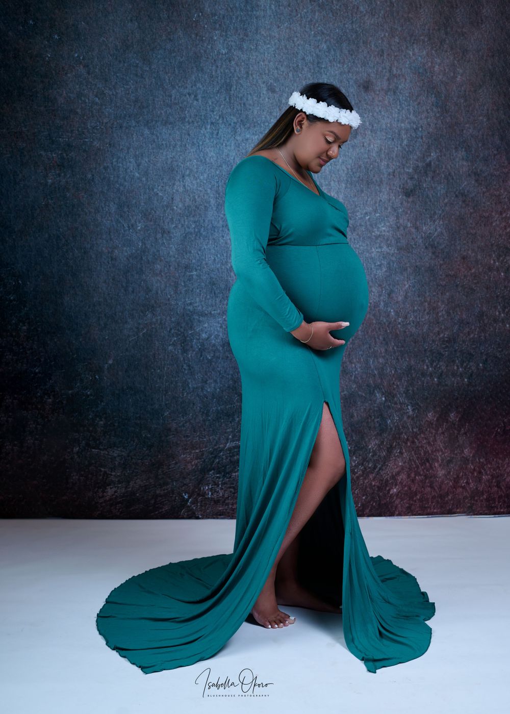 Elegant maternity portrait featuring flowing teal gown with side slit and white floral crown.