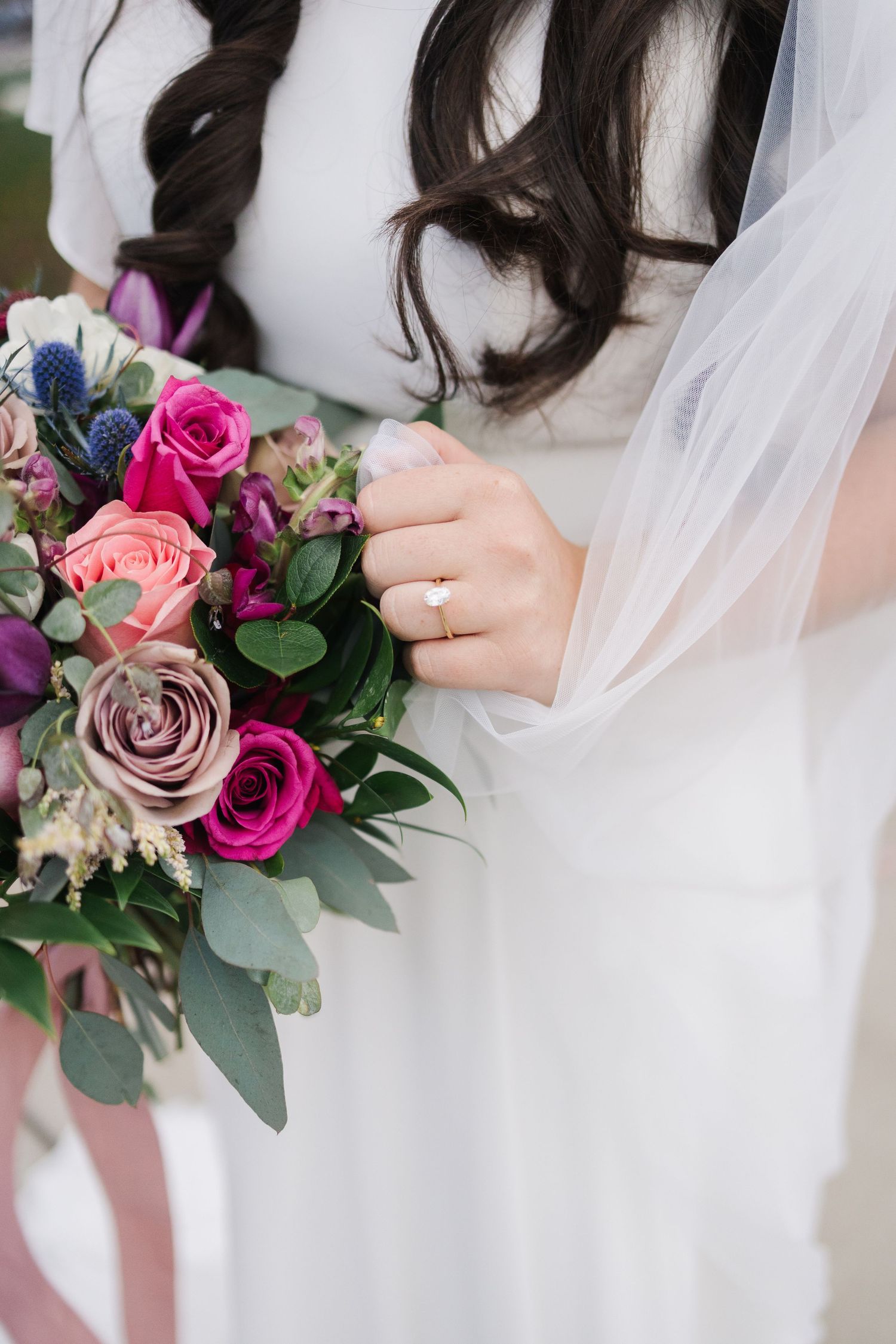 Close-up of bridal bouquet with jewel-toned roses and engagement ring detail.