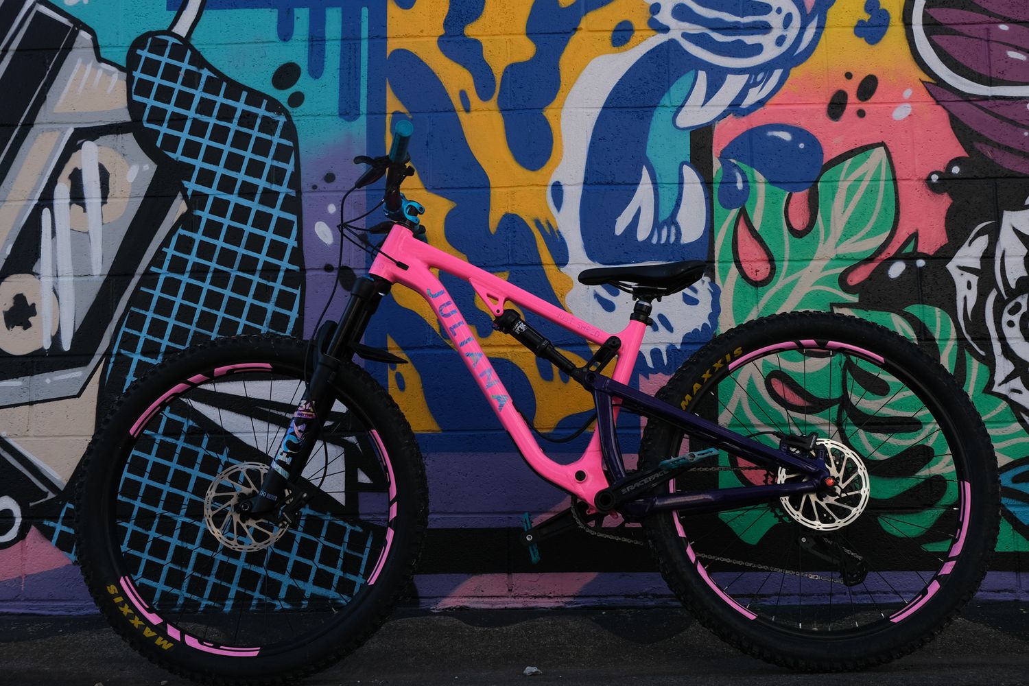 Hot pink Juliana Furtado mountain bike leans against wall art in Bentonville, Arkansas during a family lifestyle session