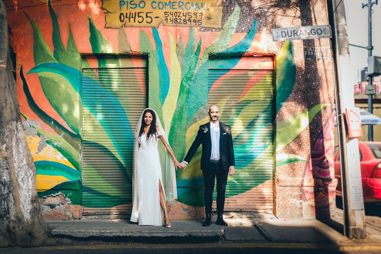 Wedding portrait against large green leaf graffiti mural on urban wall.