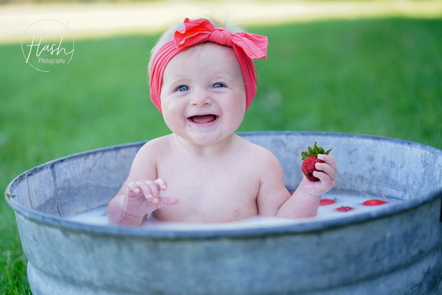 Baby wearing pink bow sitting in galvanized metal tub for bath time photos.