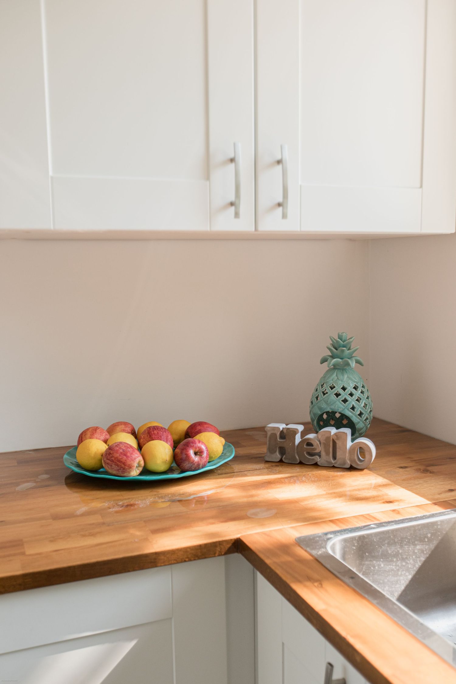 White kitchen counter with butcher block surface featuring fresh apples on a green plate and decorative pineapple.