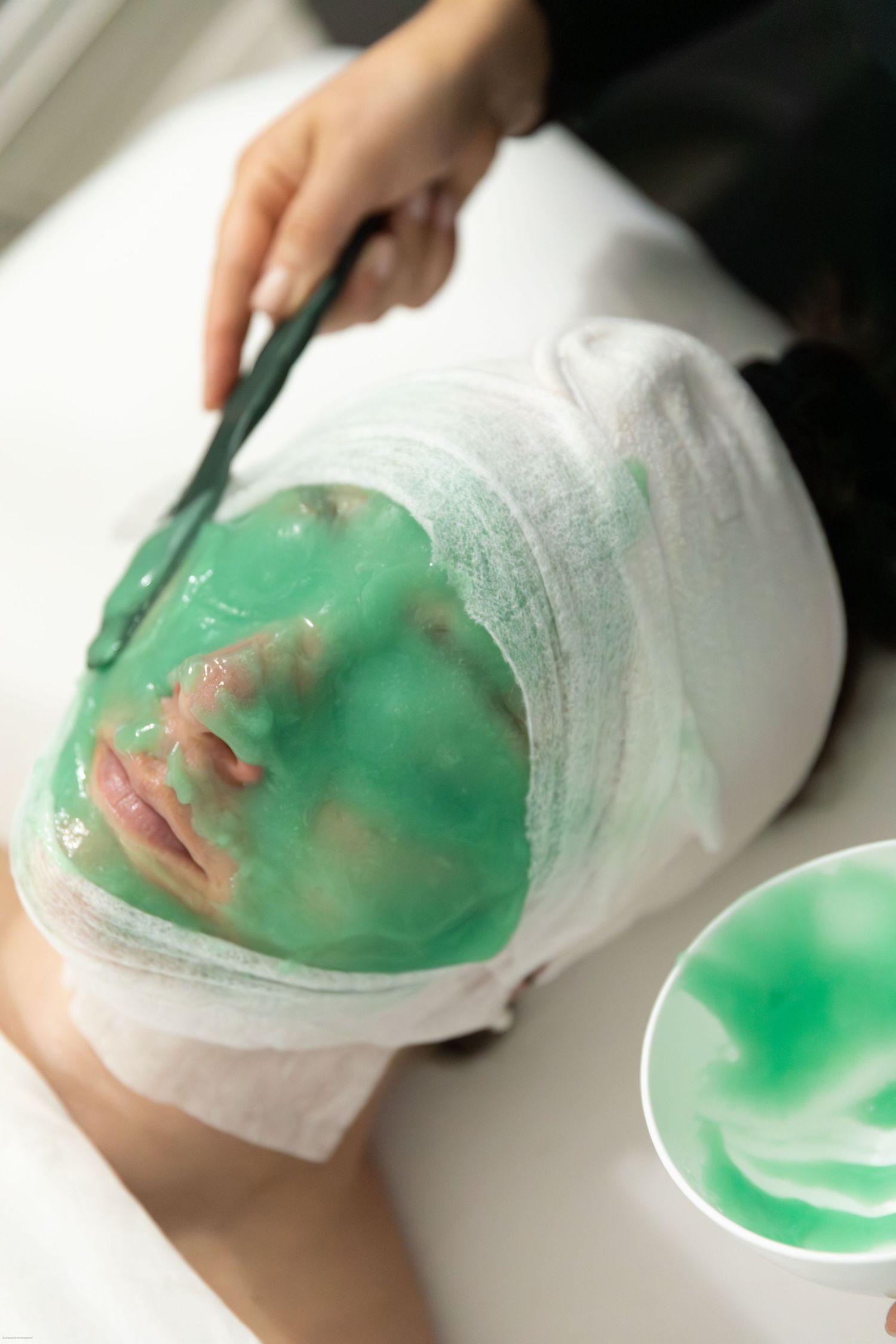 Green beauty mask being applied during professional spa facial treatment.