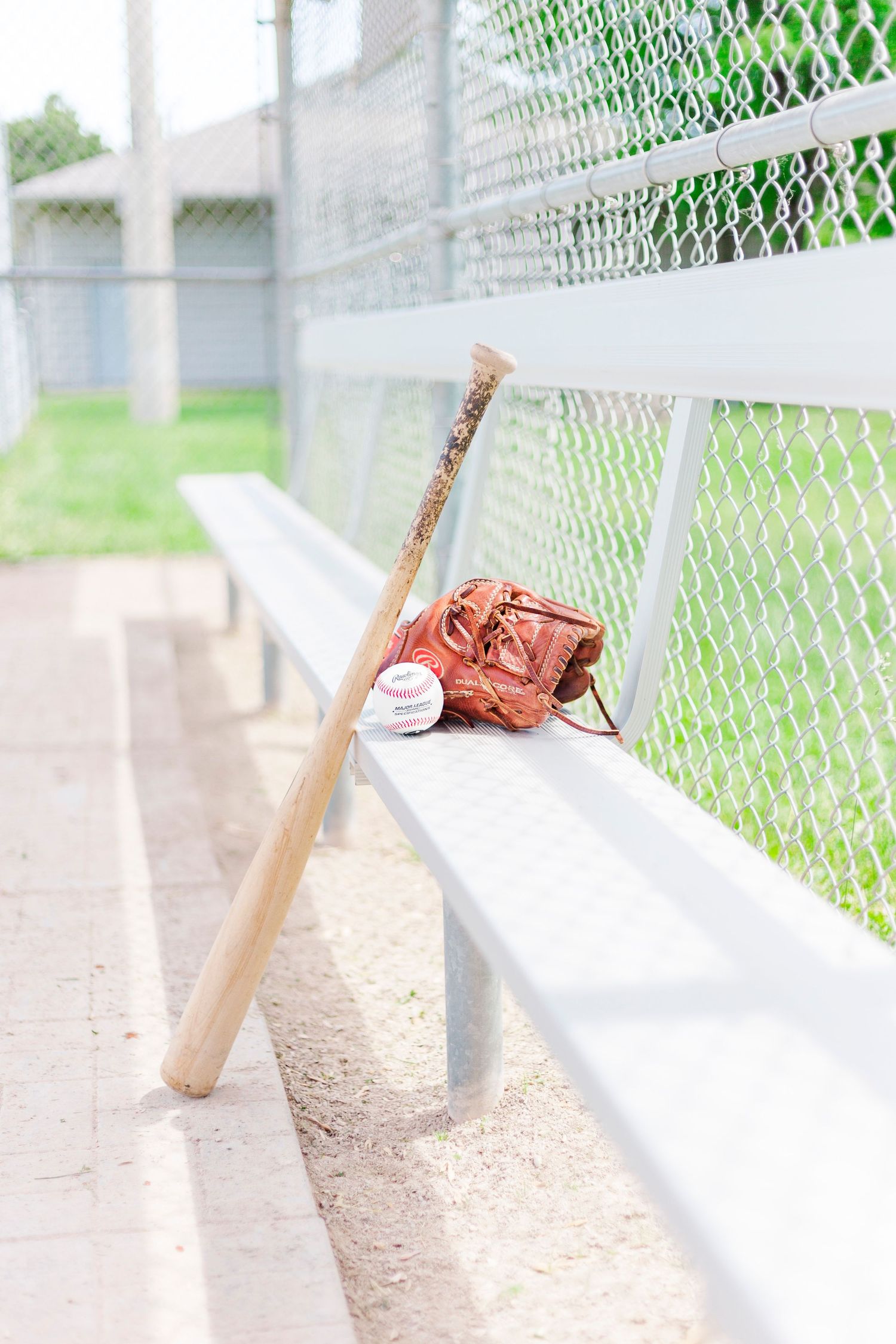 baseball brand photoshoot. baseball bat glove and ball leaving against a bench on the diamond