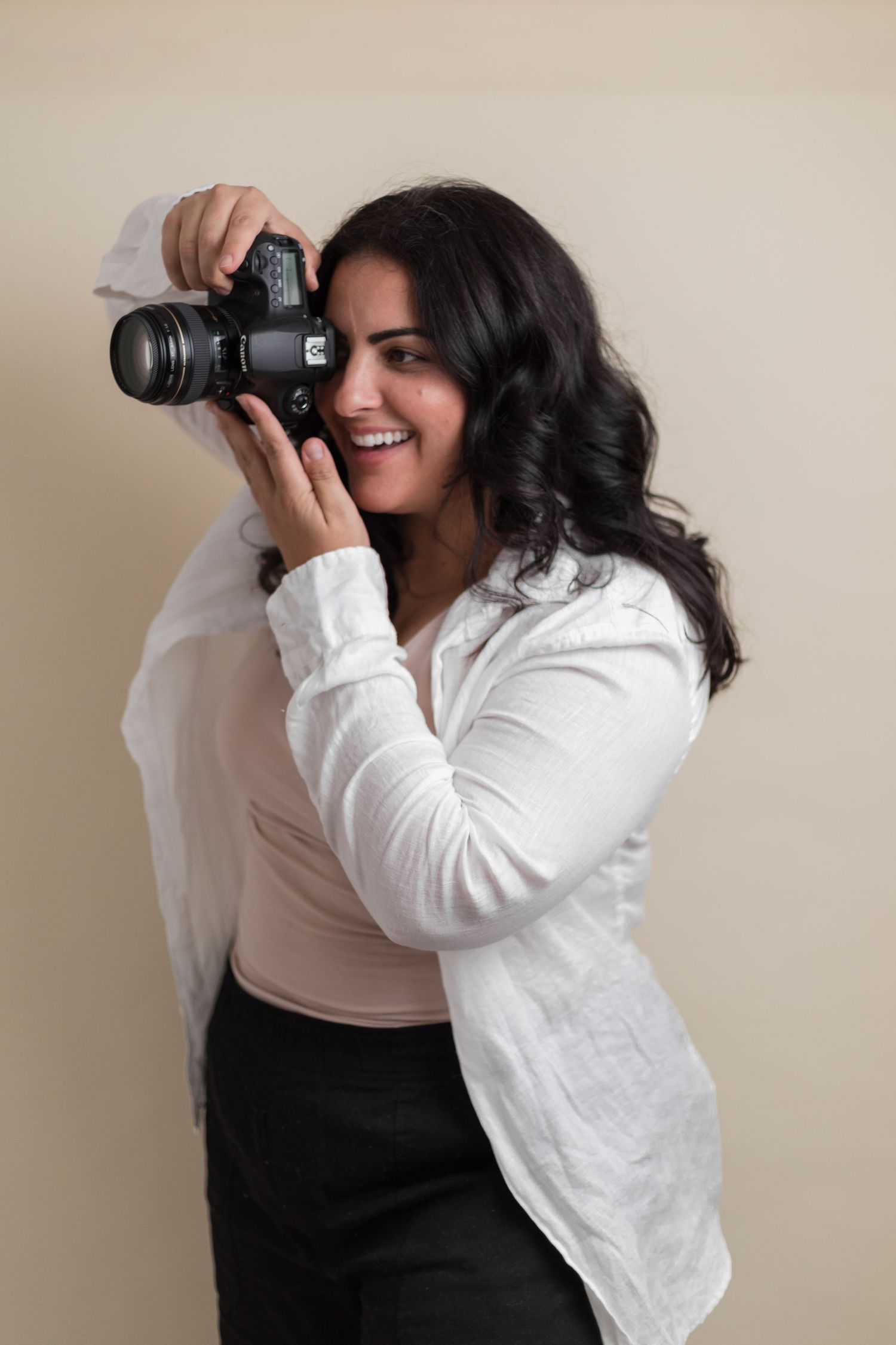Professional photographer wearing white shirt and black pants smiles while taking photos with DSLR camera.