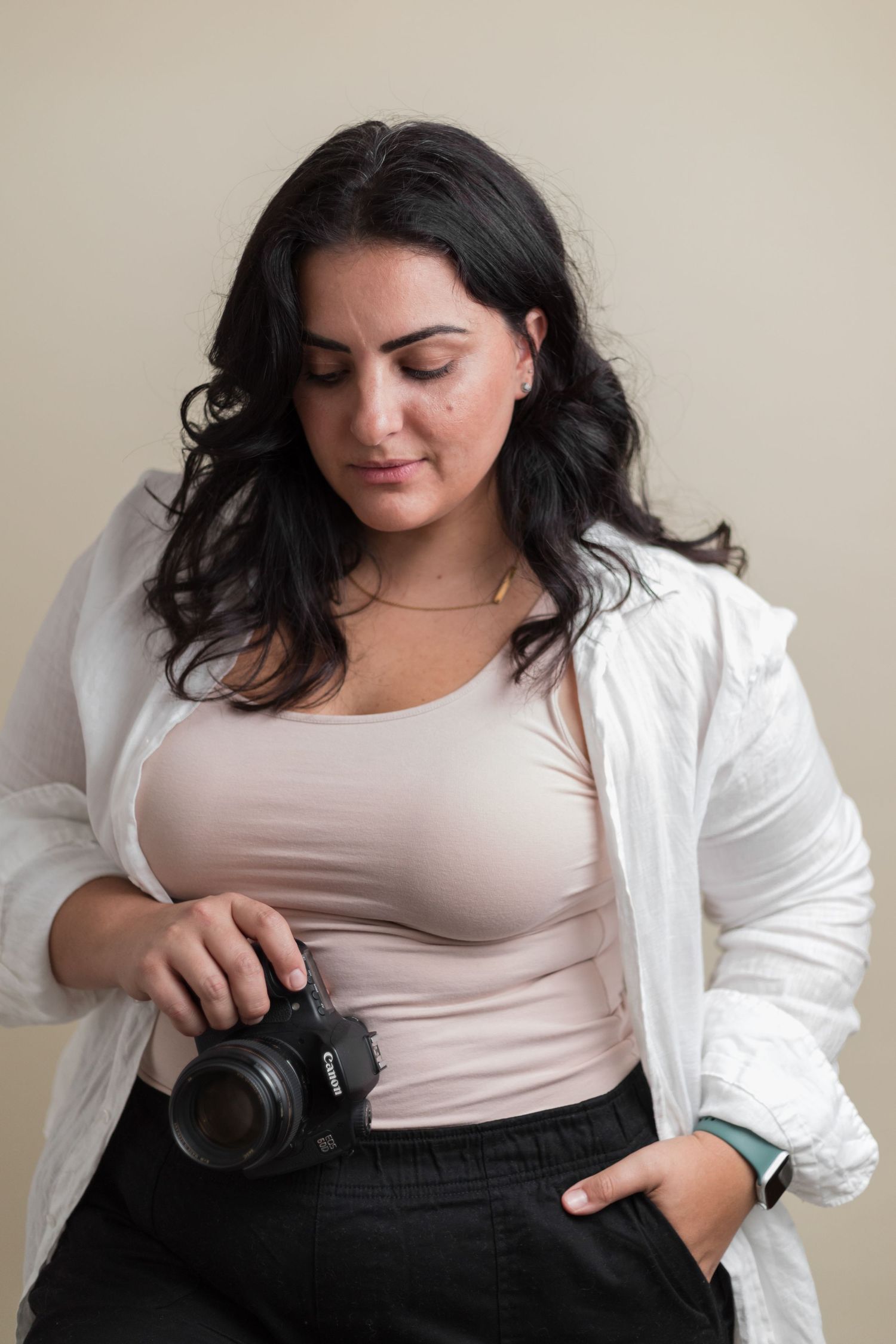 Creative photographer in casual attire poses with professional camera against neutral background.