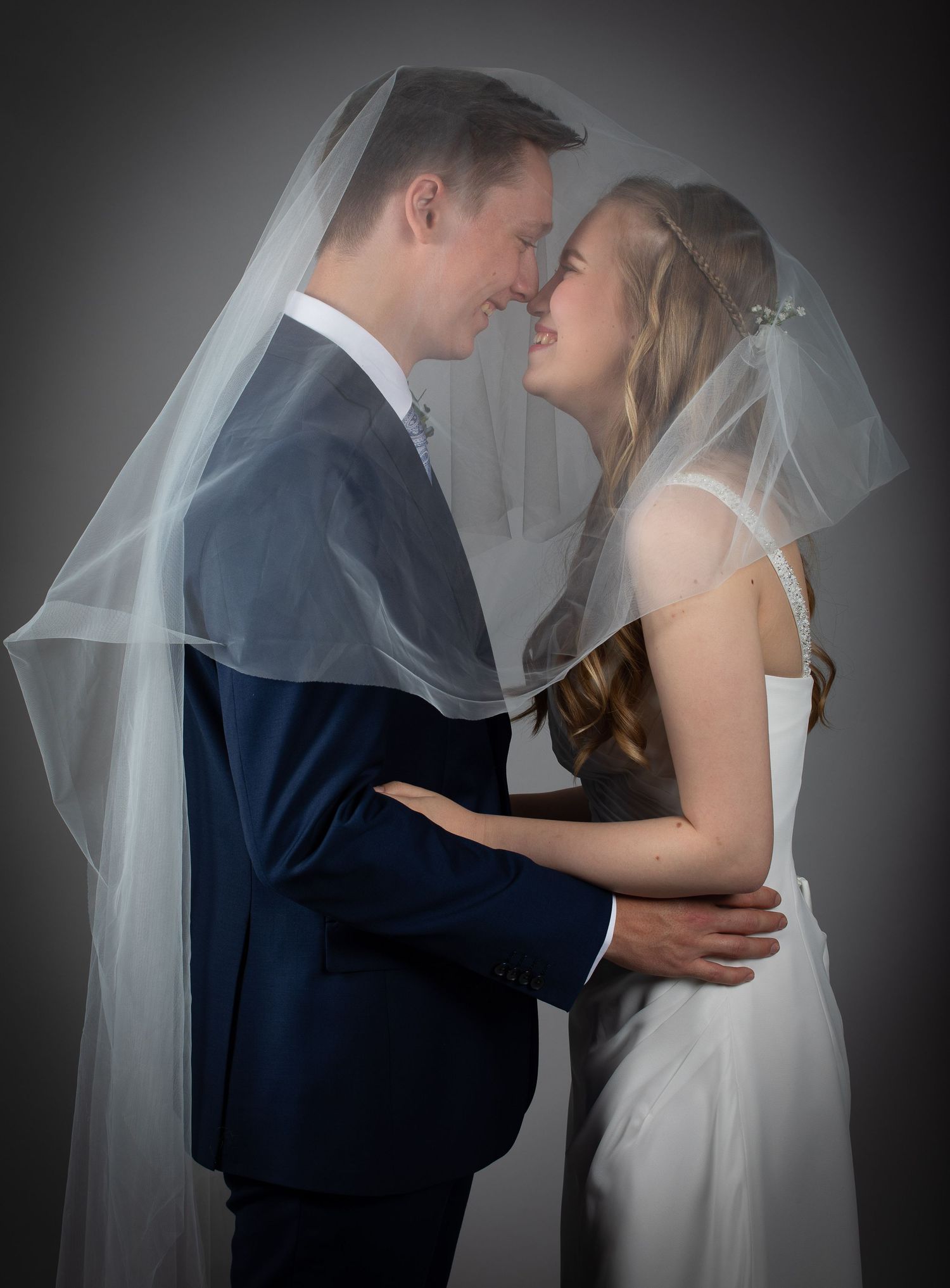 Romantic bride and groom sharing an intimate moment under a flowing white wedding veil.