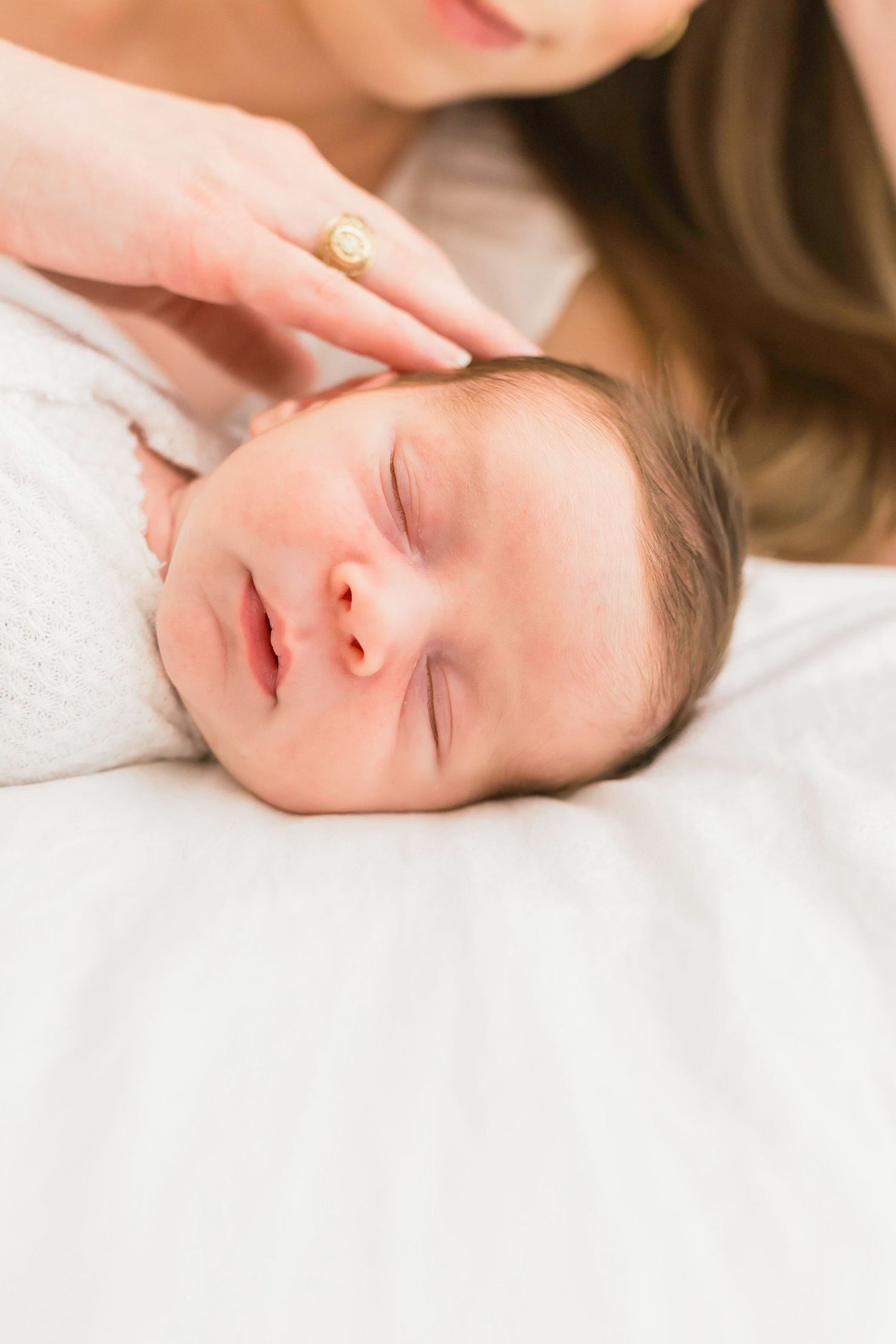 Close-up of sleeping newborn baby with gentle touch on head.