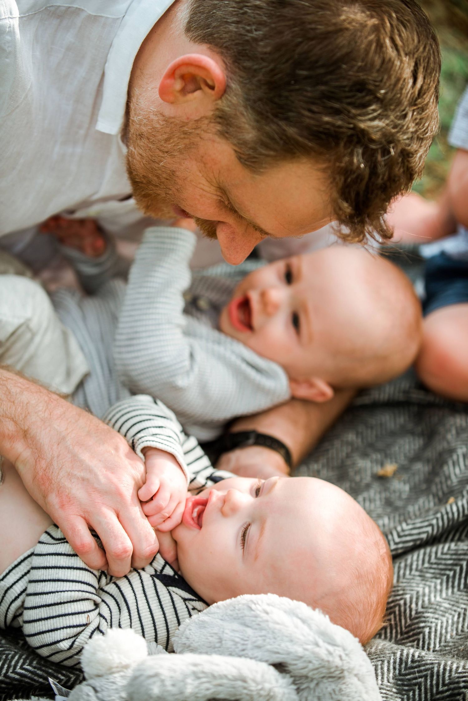 Tender family moment captured on a grey blanket outdoors with twins in matching striped outfits.