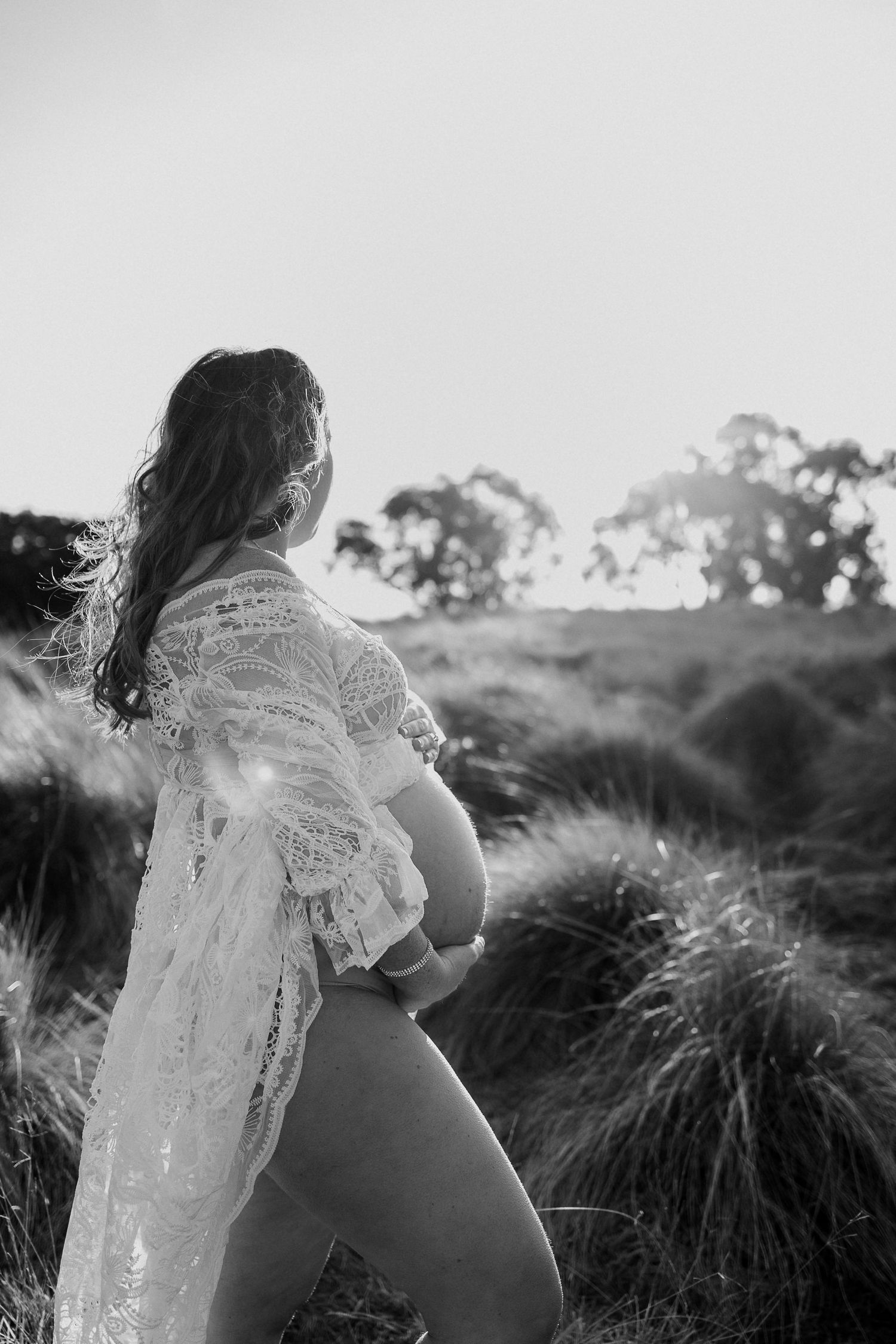 Silhouette of woman in lace dress standing in field during golden hour.