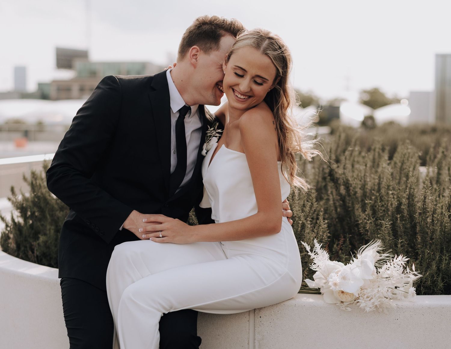 Newlywed couple shares a joyful moment together on their wedding day against an urban backdrop.