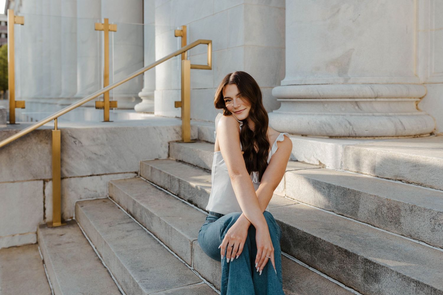Woman in casual outfit sitting on marble steps with ornate handrail.