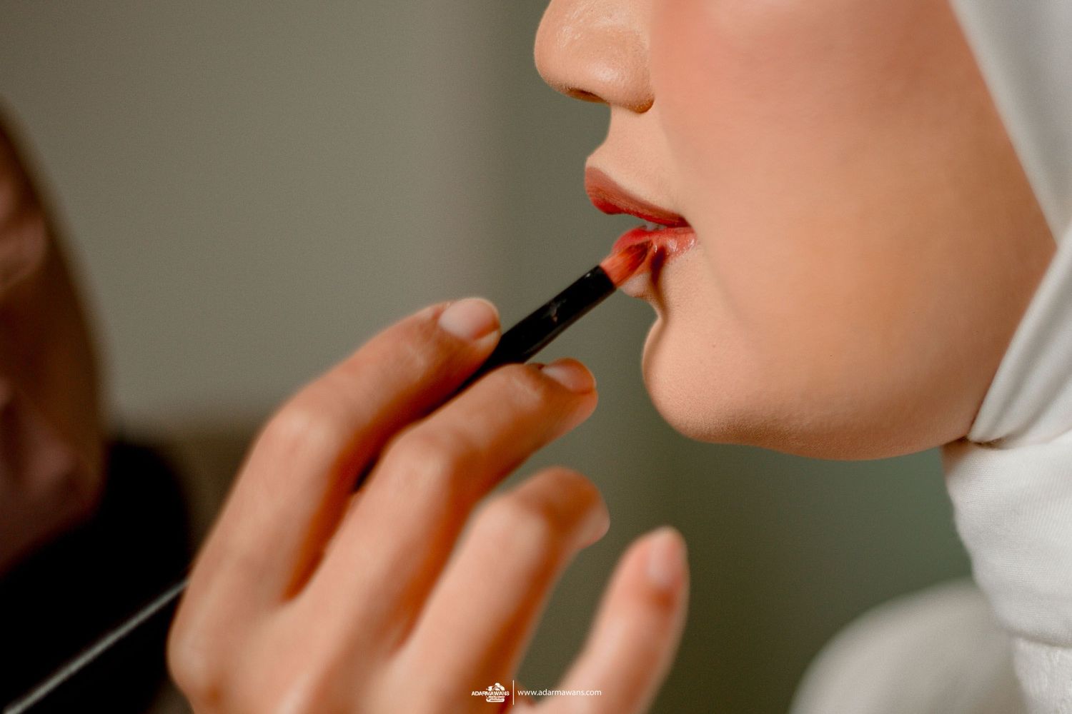 Close-up shot of applying red lipstick on a person wearing a white hijab.