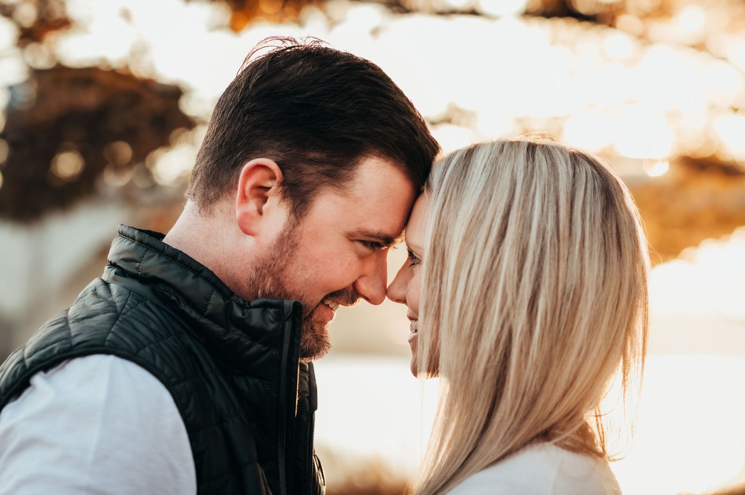 husband and wife lean foreheads together with orange sunset behind them through fall leaves in Chattanooga