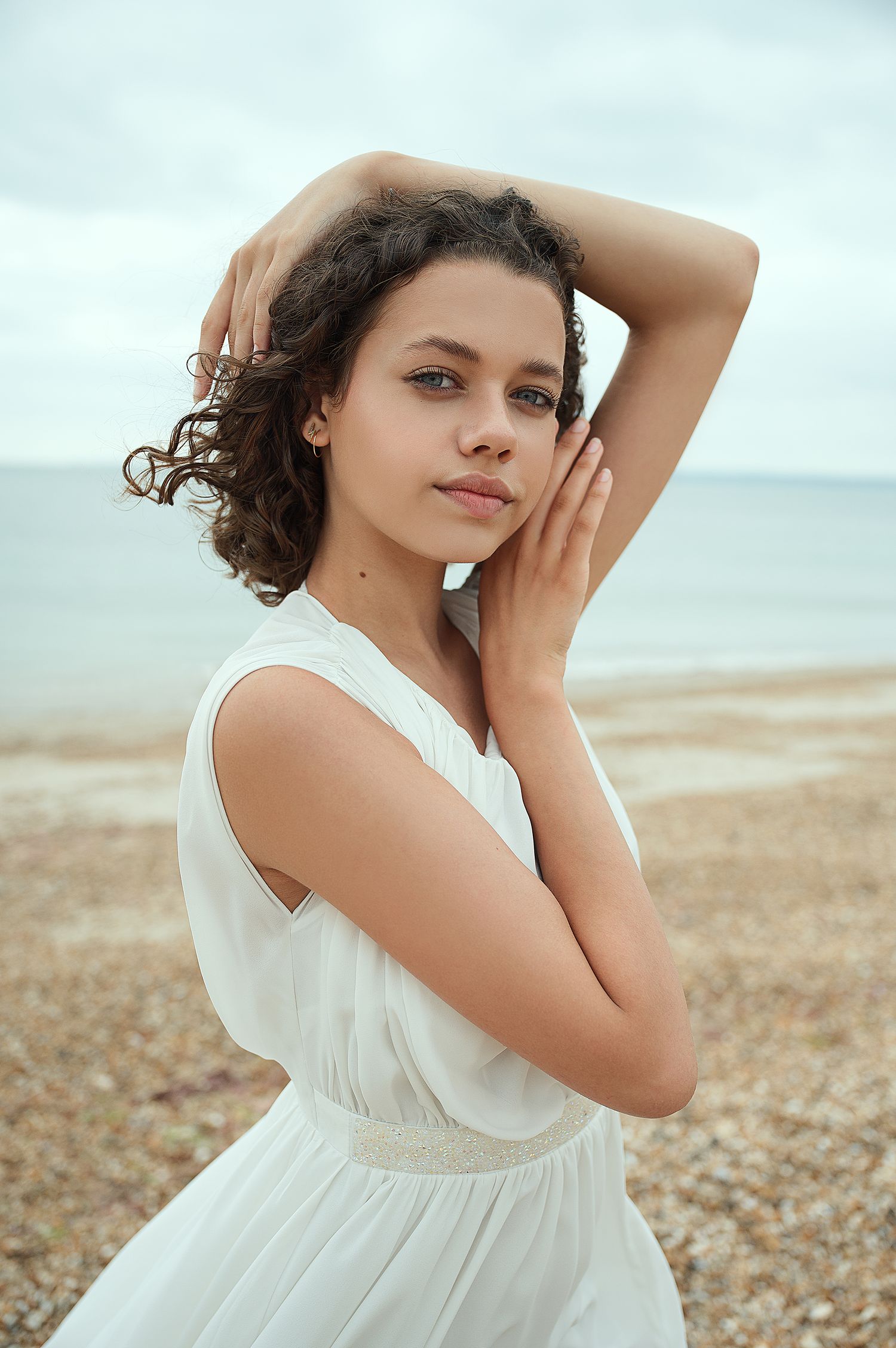 Beachy portrait in flowing white dress on pebbled shoreline.