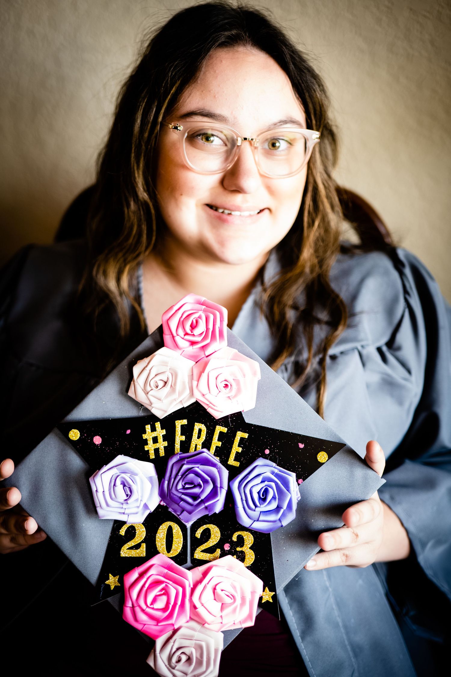 Smiling graduate portrait holds decorated cap  adorned with colorful fabric roses.