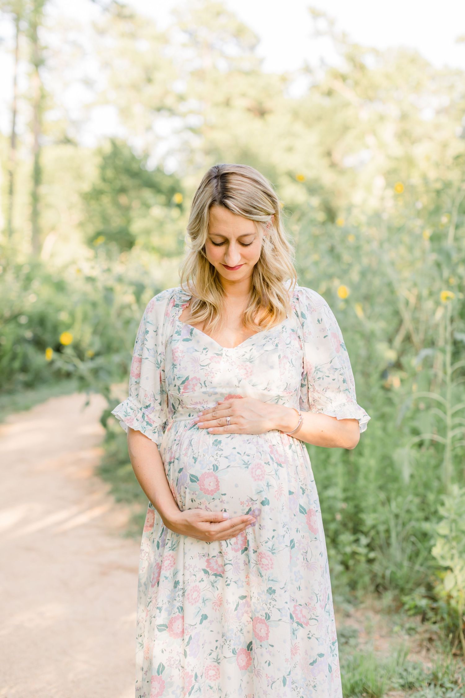 Romantic maternity portrait in floral dress against natural outdoor backdrop.