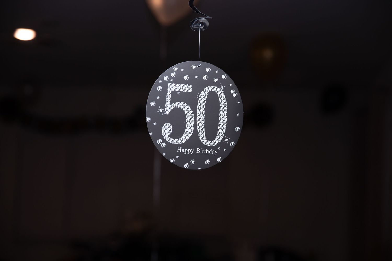 A black and silver balloon with the number 50 printed on it hangs in a dark space against a blurred background.