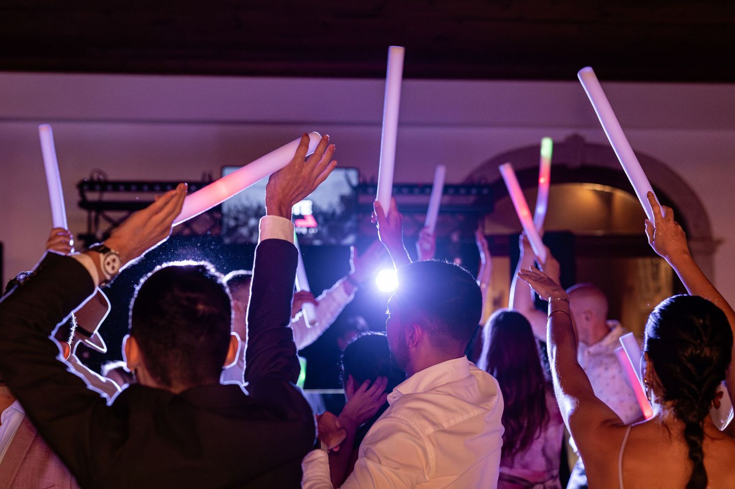 Concert crowd waves light-up glow sticks in the air during a nighttime performance with blue spotlights illuminating the scene.