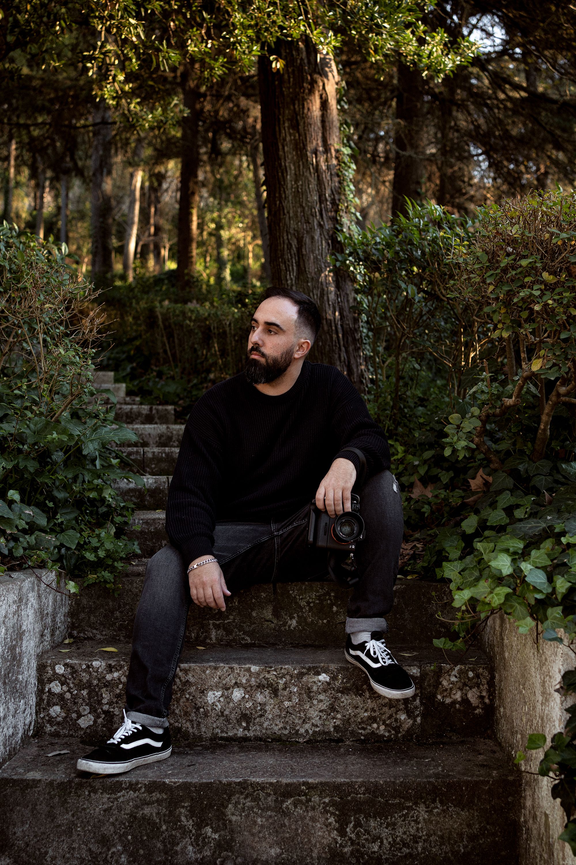 Person in black clothing sitting on concrete steps in a wooded area.