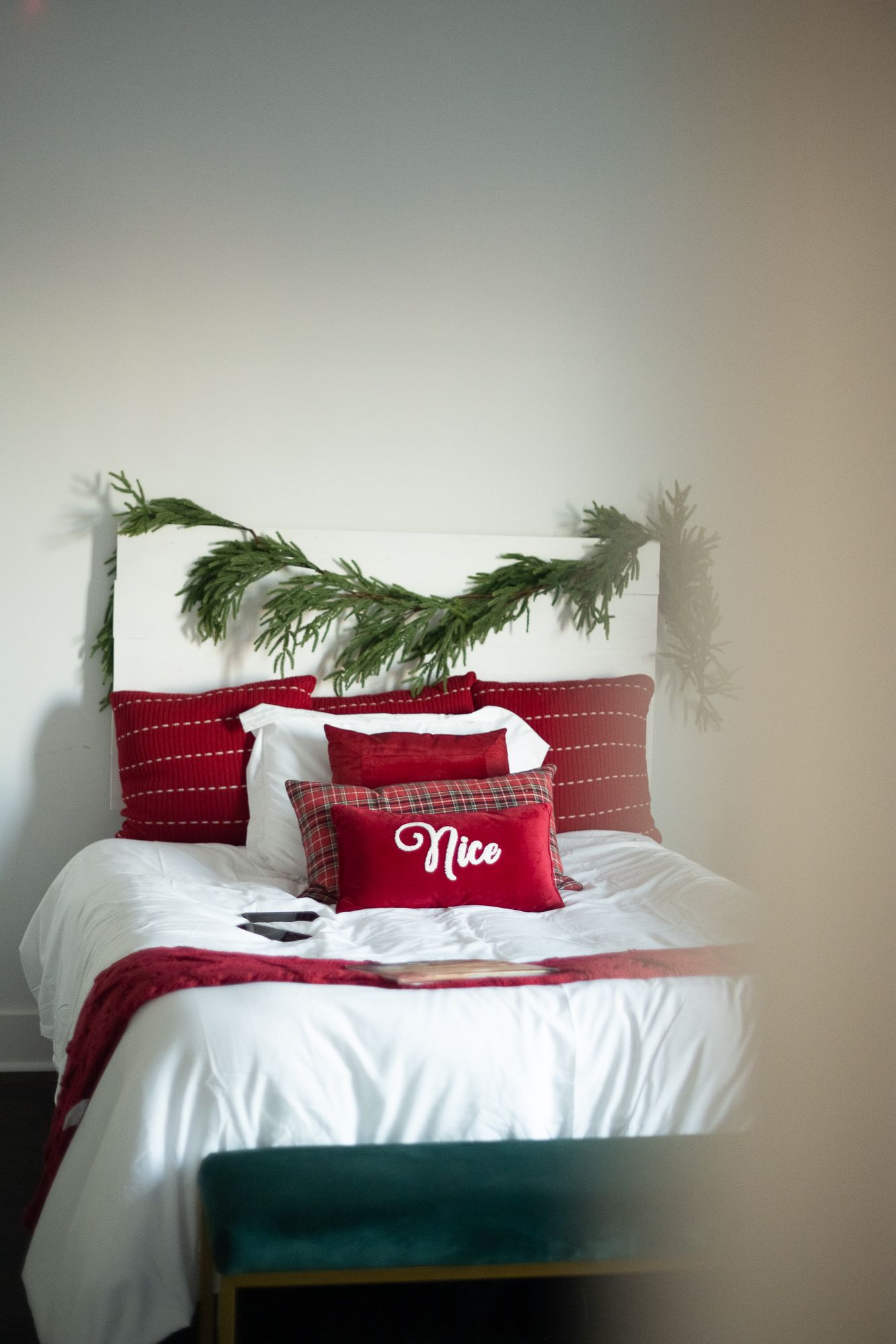 A festive bed with red and white bedding, holiday greenery, and a 'Nice' pillow.