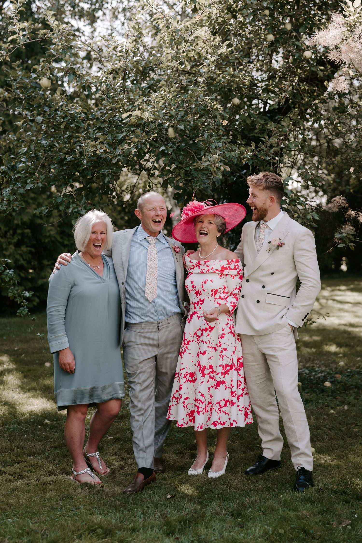 groom with family laughing for a portrait in orchard in islip, oxfordshire