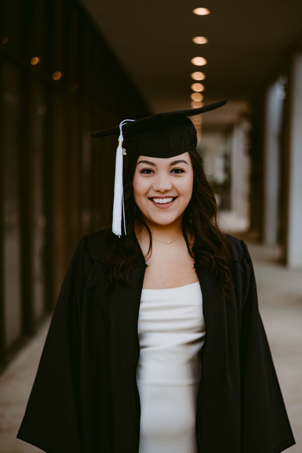 Graduate wearing traditional black graduation cap with tassel poses in indoor hallway.