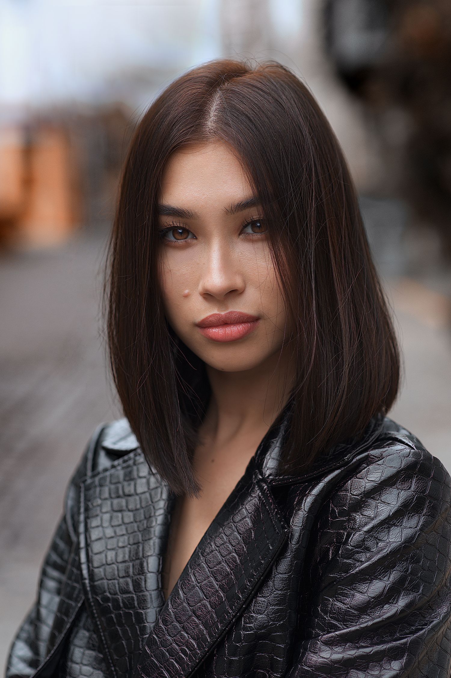 Fashion portrait of a person wearing black leather jacket with long dark hair against blurred background.