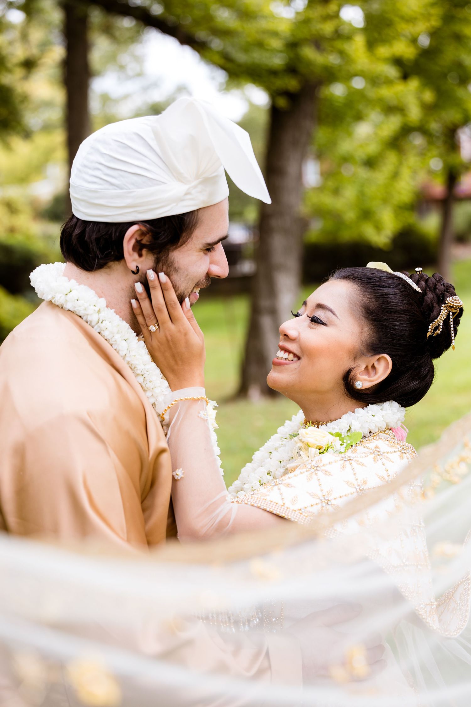 Couple in traditional Burmese wedding attire sharing romantic moment outdoors.