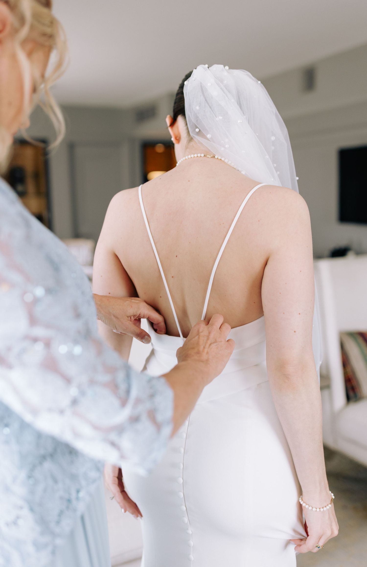 Close-up of bride's back showing delicate spaghetti strap dress details while getting ready.