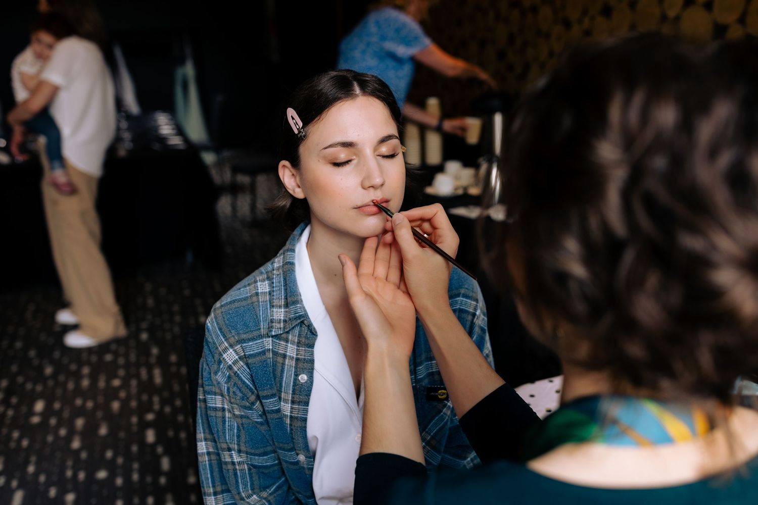 A makeup artist applying cosmetics in a dimly lit room.