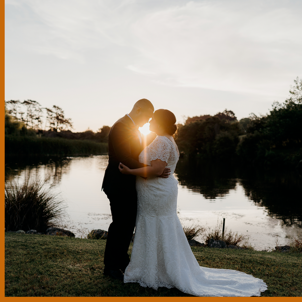bride and groom touching foreheads while hugging at sunset in front of a lake