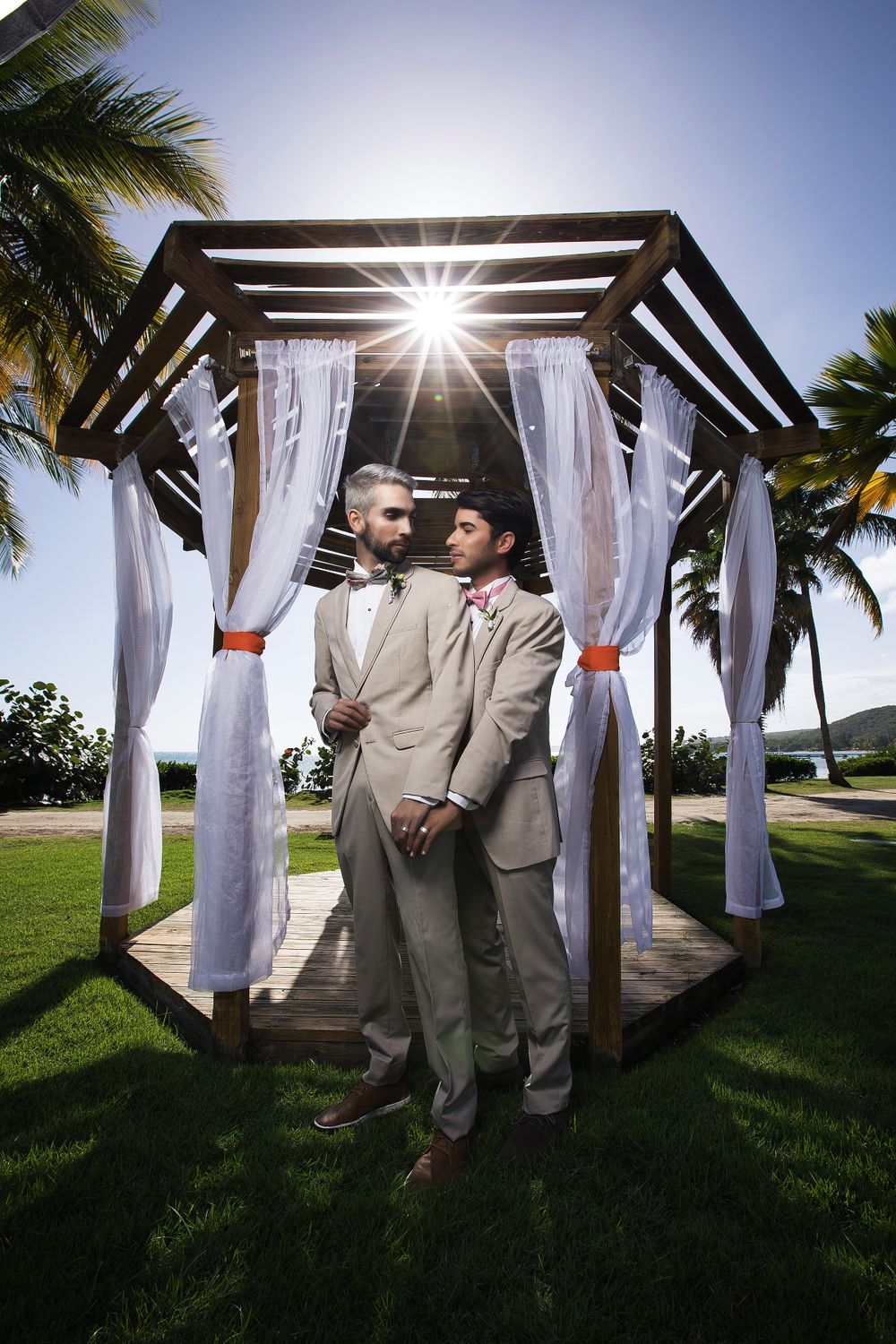 Wedding ceremony setup with white draped pergola and sunburst through the slats.