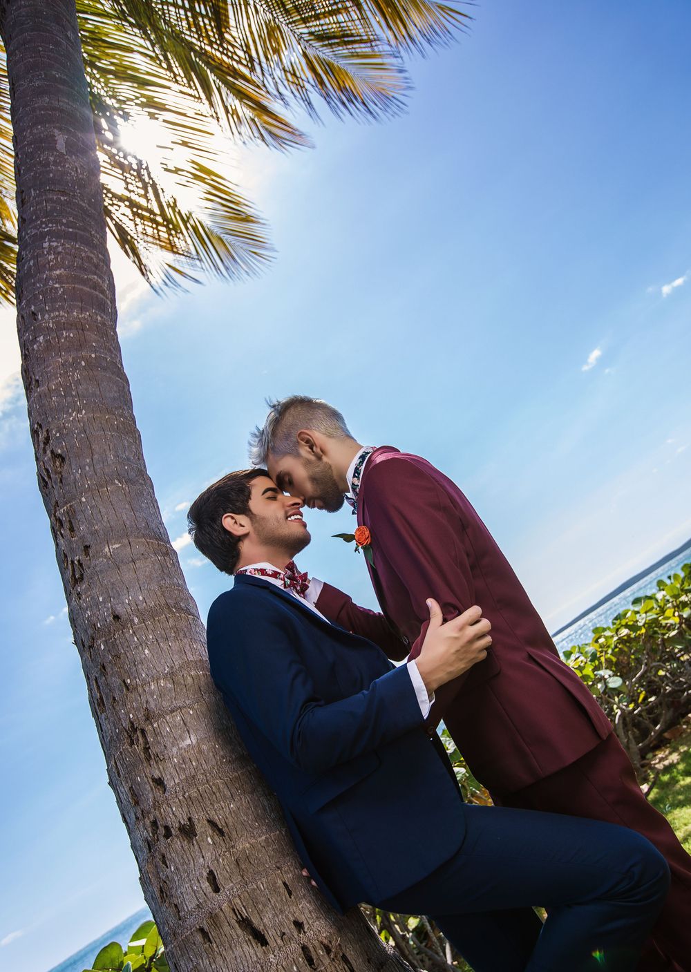 Romantic moment under a palm tree on a tropical beach with bright blue sky.