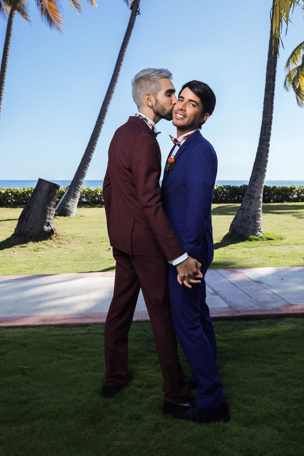 Intimate moment shared between a couple in formal attire near palm trees by the ocean.