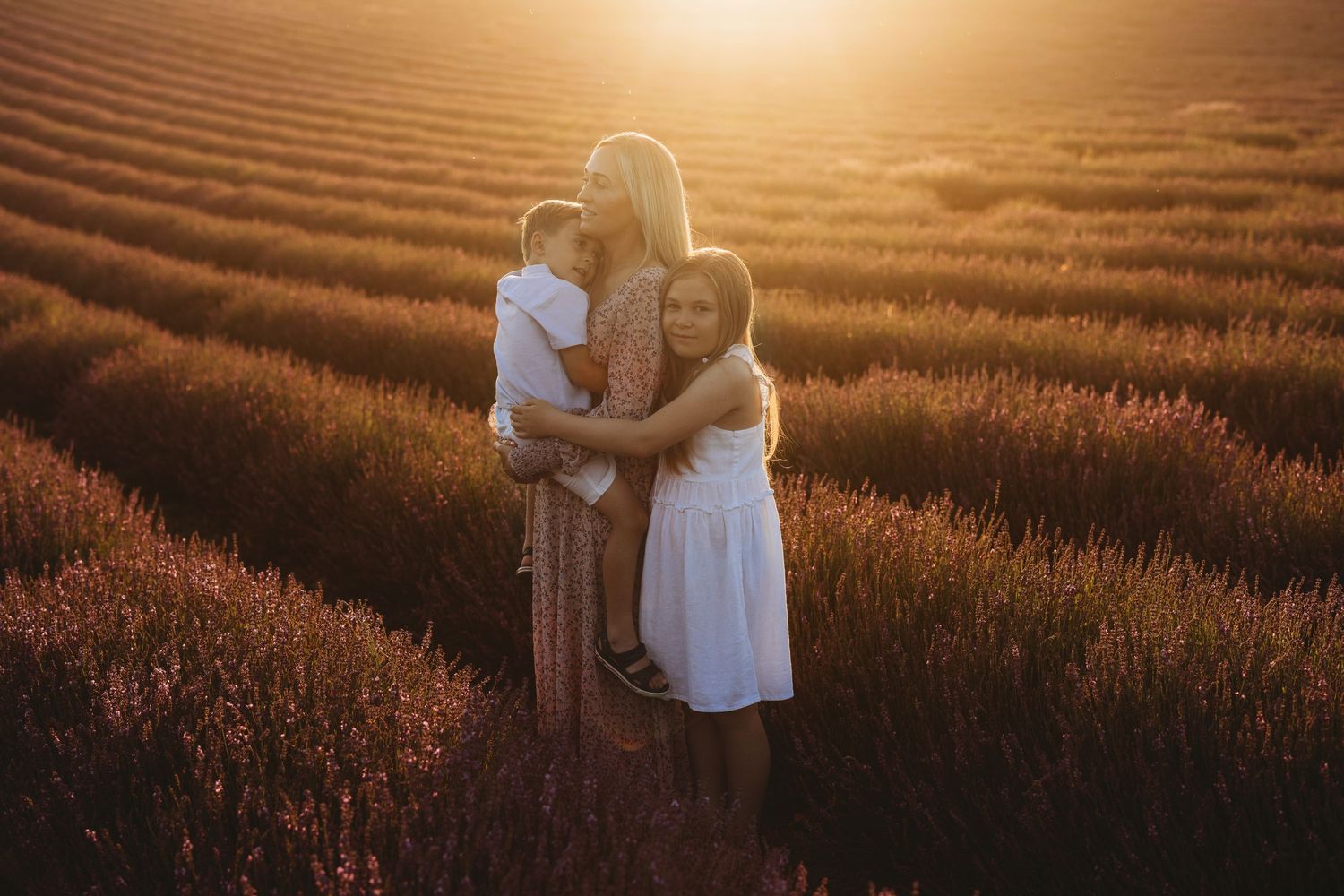 Family embracing in golden wheat field during sunset.