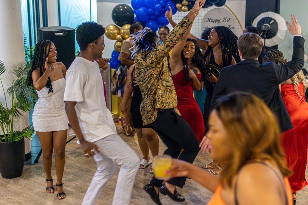 Party guests dancing and celebrating among blue and gold balloon decorations.