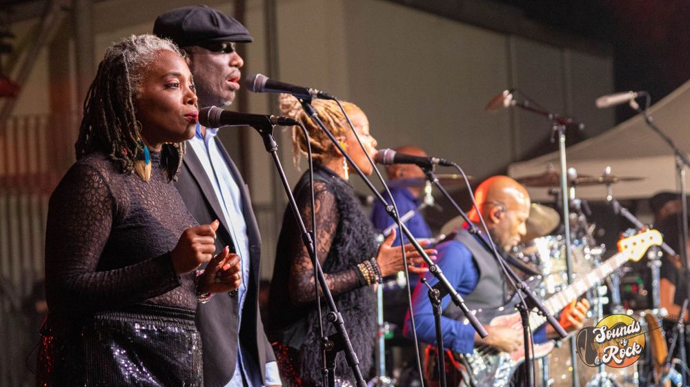 Multiple singers performing in harmony on stage during live musical performance.