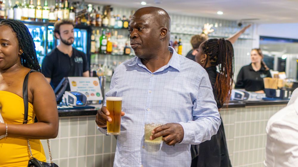 Diverse group of patrons socializing at a well-stocked bar counter during an event.