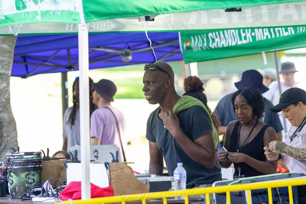 Vendors serving customers under blue and green tents at outdoor festival.
