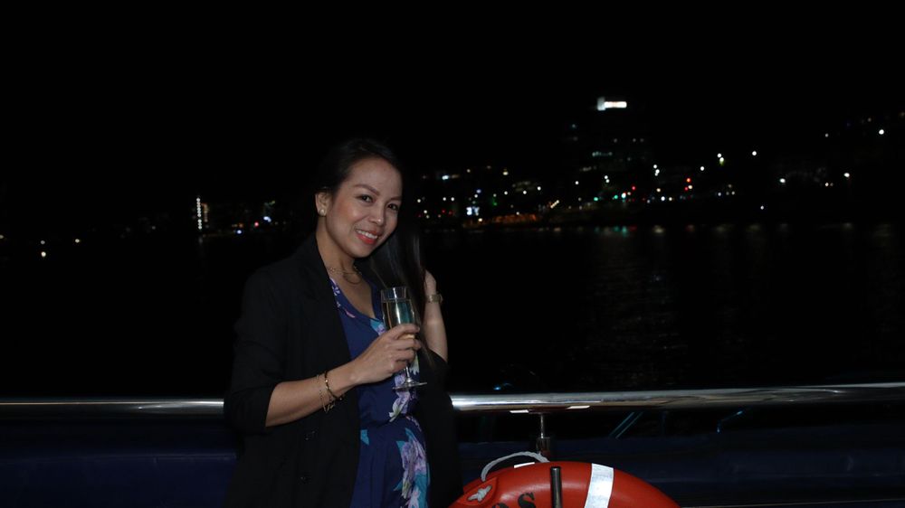 A guest with a beverage poses on a dark waterfront terrace.