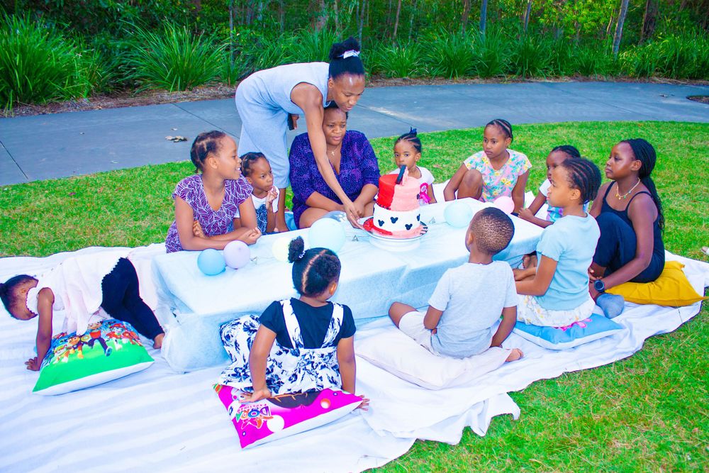A festive outdoor gathering with people seated on blankets enjoying cake together.