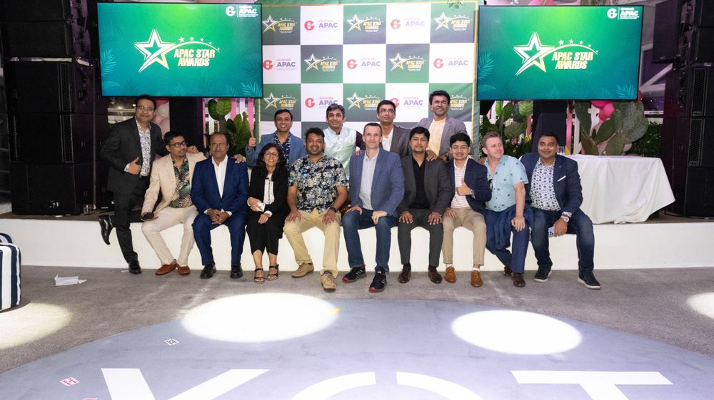 Professional group seated together for formal photo with green branded backdrop and spotlights.