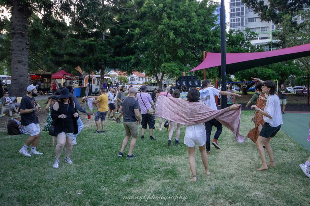Crowd of people dancing and socializing at outdoor park event.