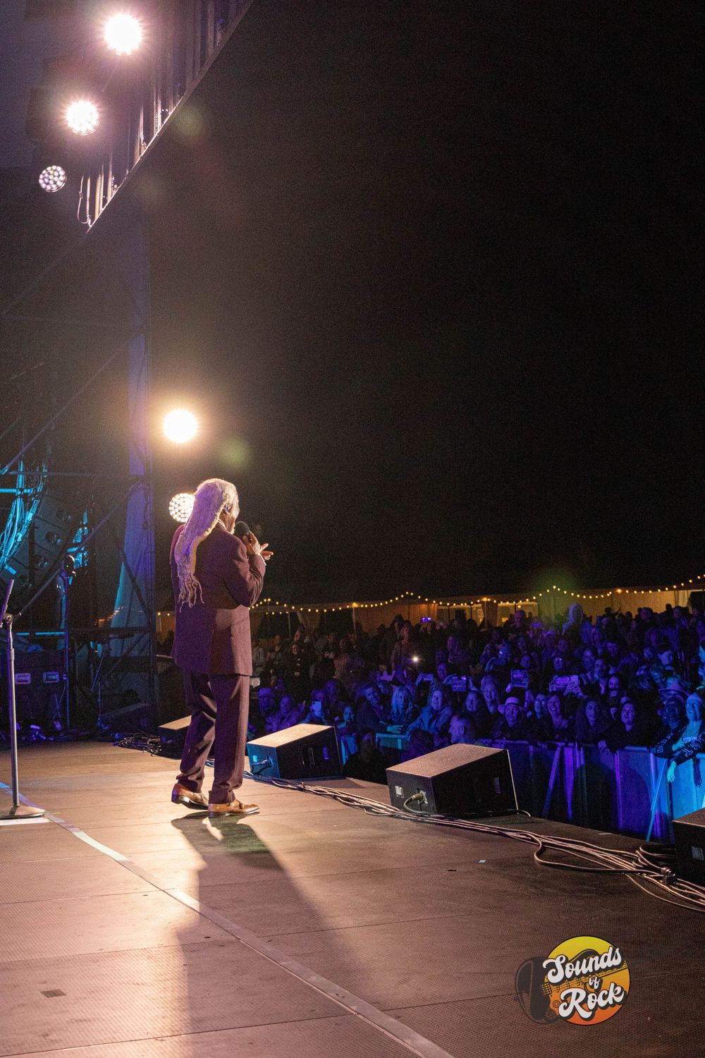 Solo performer on elevated stage with crowd visible in blue lighting below.