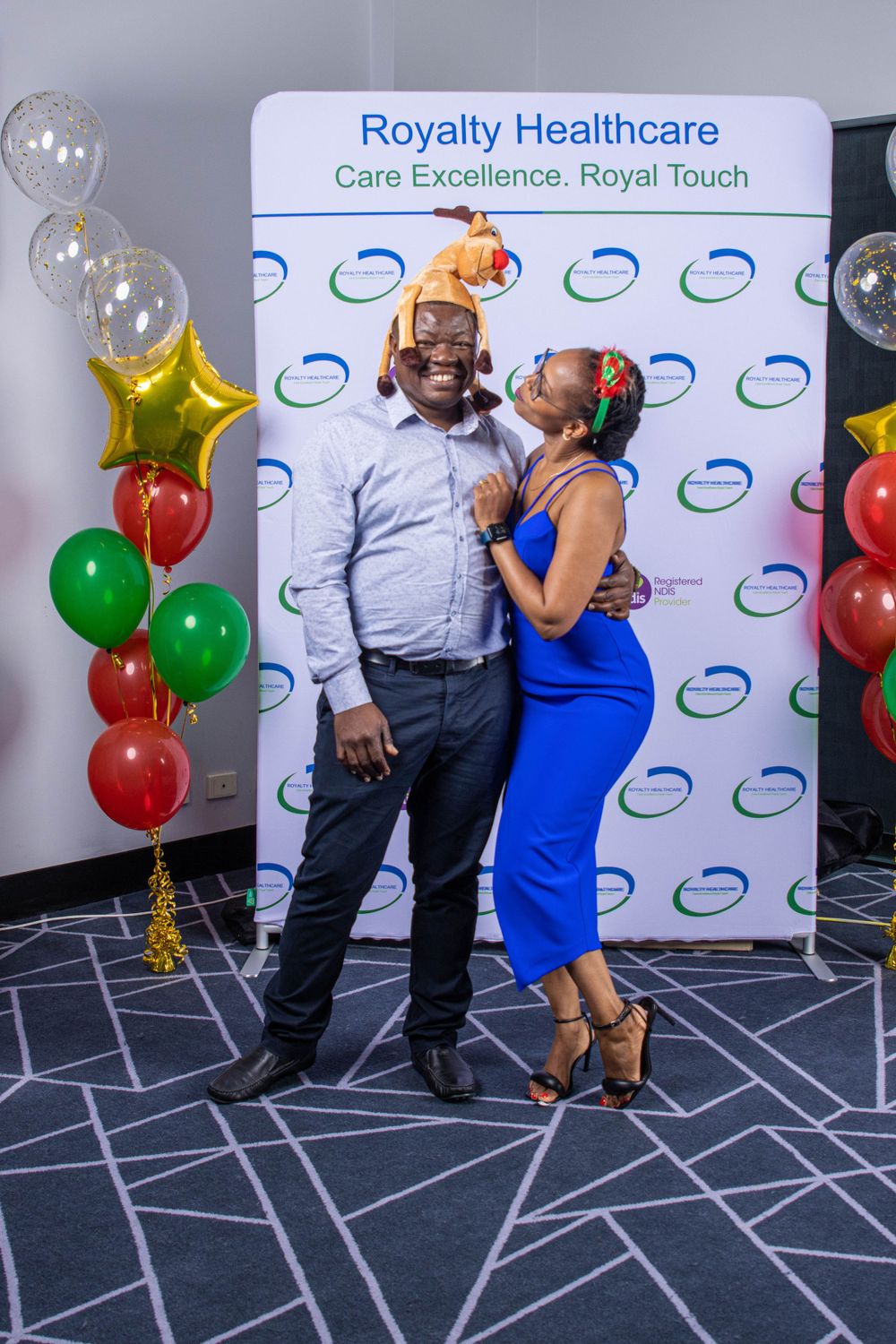 A couple poses at a Royalty Healthcare event with balloons and a branded backdrop.