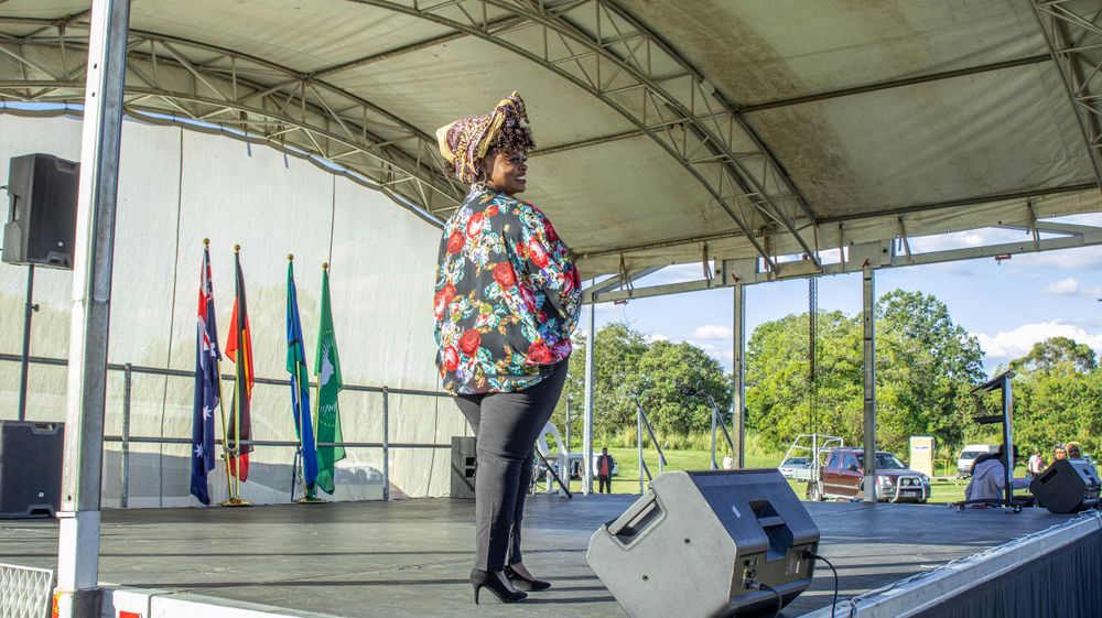 Solo performer in floral print top singing on covered outdoor stage.