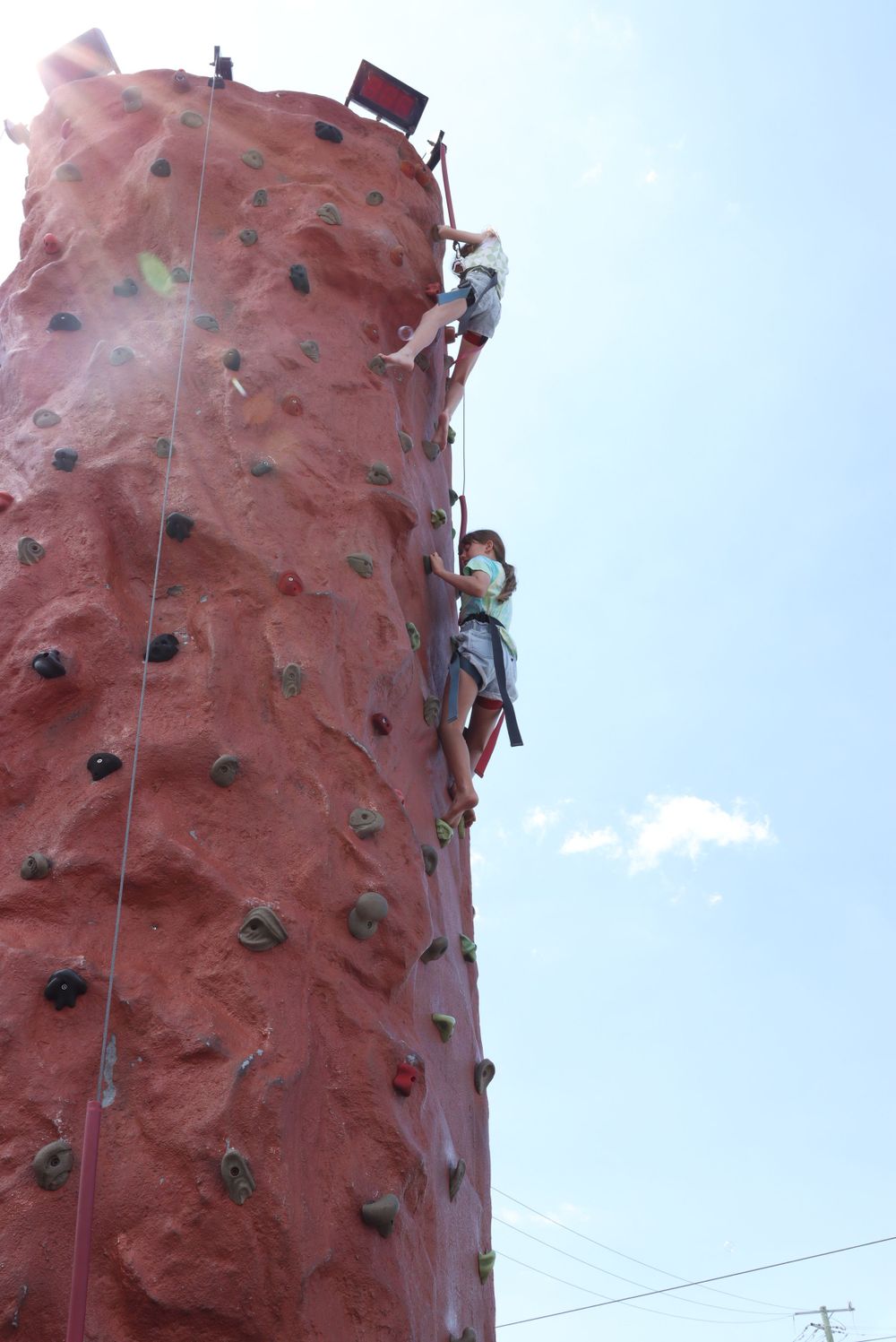 Multiple climbers scaling a large outdoor climbing wall against clear blue sky.