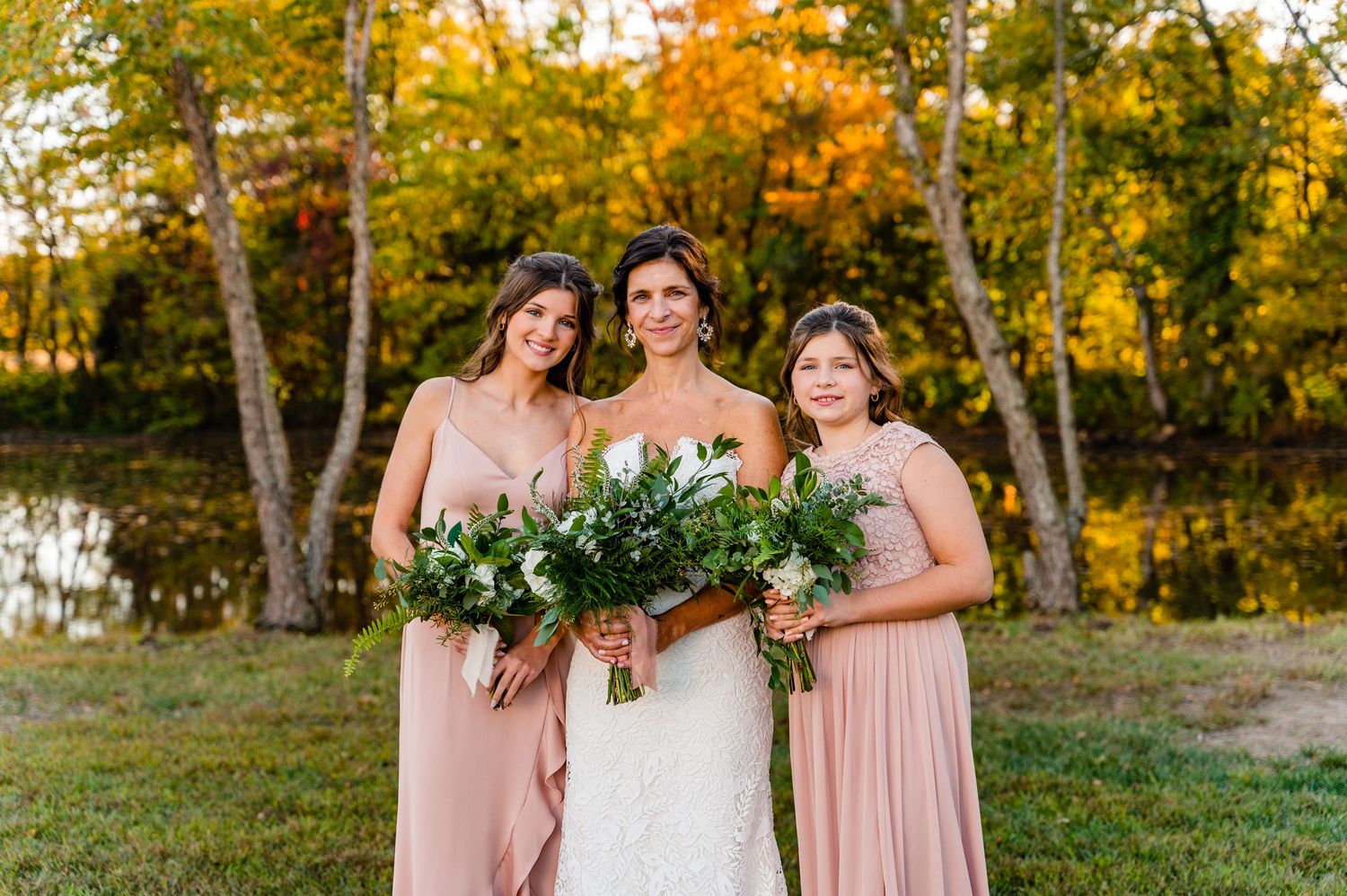 woman in wedding dress with two girls on either side in light pink, long dresses